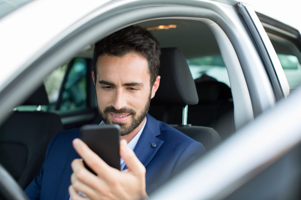 Young businessman reading smartphone texts in car