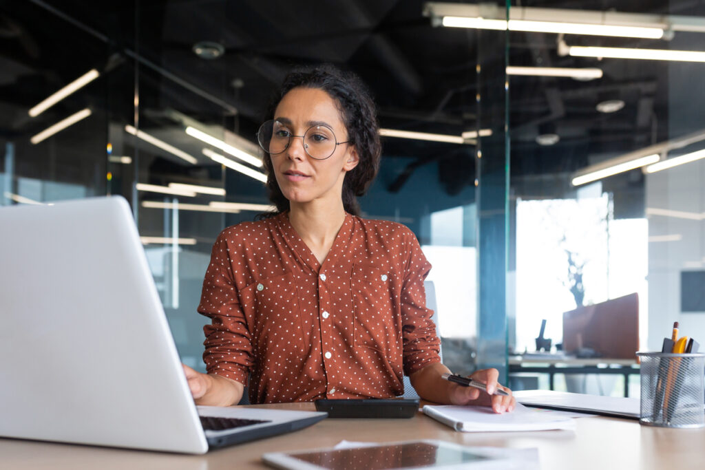 Successful satisfied and happy business woman working inside modern office, hispanic woman in glasses and shirt using laptop at work,